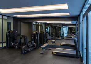 Un gimnasio moderno con diverso equipamiento de ejercicio, incluyendo cintas de correr y máquinas de pesas, y amplias ventanas que proporcionan luz natural.