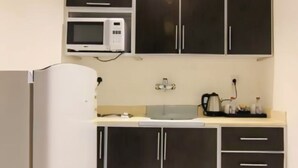 Eine kleine Küche mit dunklen Schränken, einer Mikrowelle, einem Kühlschrank und einer Kaffeemaschine.