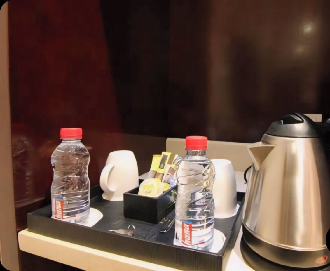 De minibar van een hotelkamer met een waterfles, koffiekop en een zilveren elektrische waterkoker.