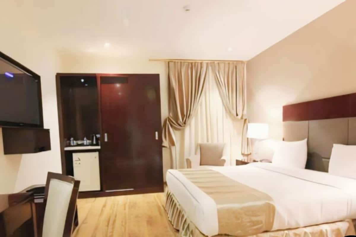 Quarto de hotel com cama, mesas de cabeceira, escrivaninha, televisão e guarda-roupa.