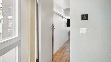 Un pasillo con una puerta que da a una habitación, una ventana y un termostato en la pared.
