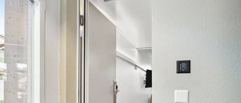 Un pasillo con una puerta que da a una habitación, una ventana y un termostato en la pared.