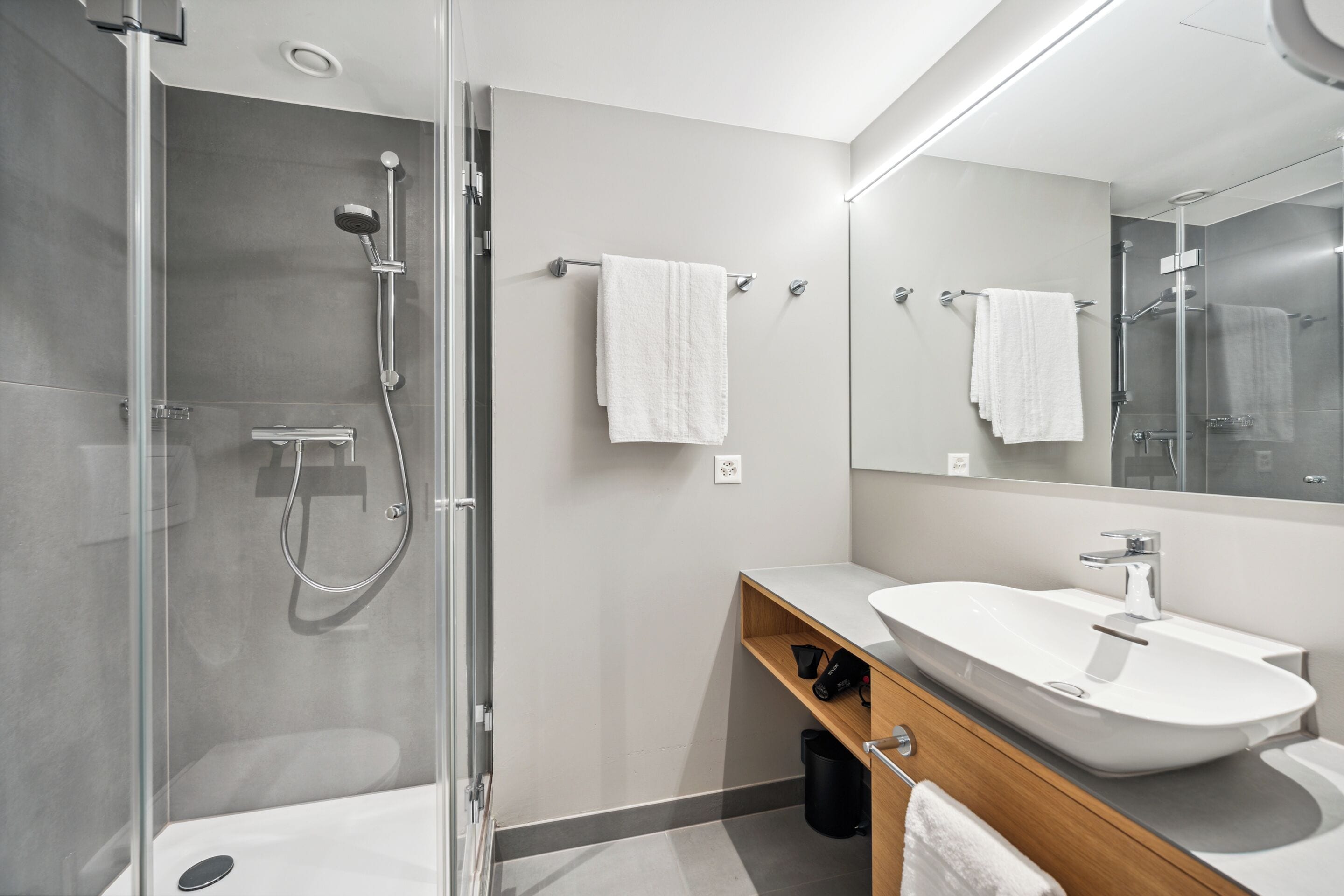 A modern bathroom with a glass-enclosed shower, a white sink, and a mirror above the vanity.