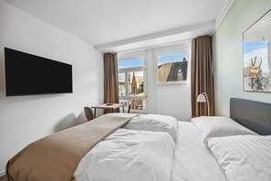 Habitación de hotel con dos camas, un escritorio, un televisor y una ventana con vista a edificios.