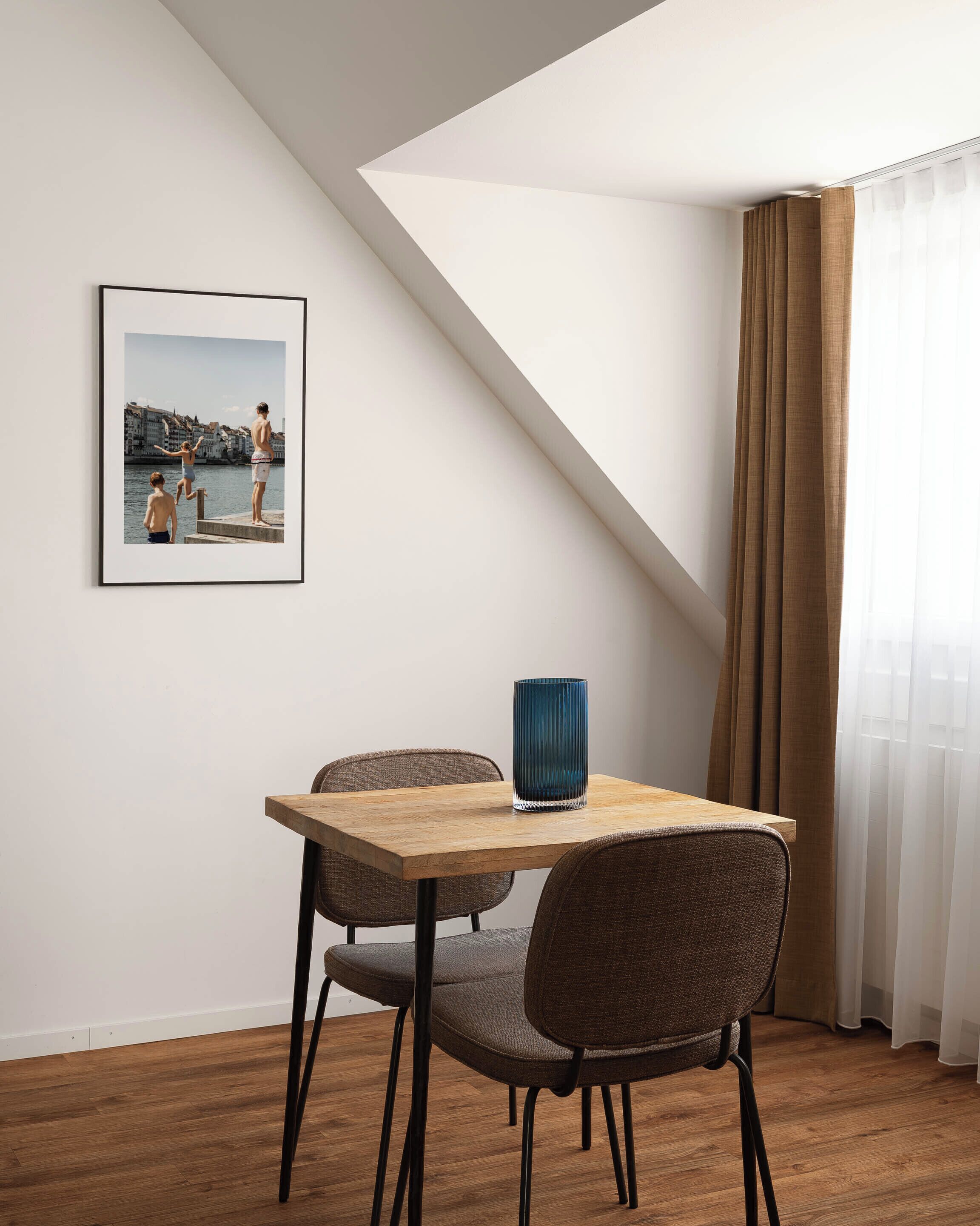 A dining area with a table, chairs, a framed photograph, and a window with curtains.