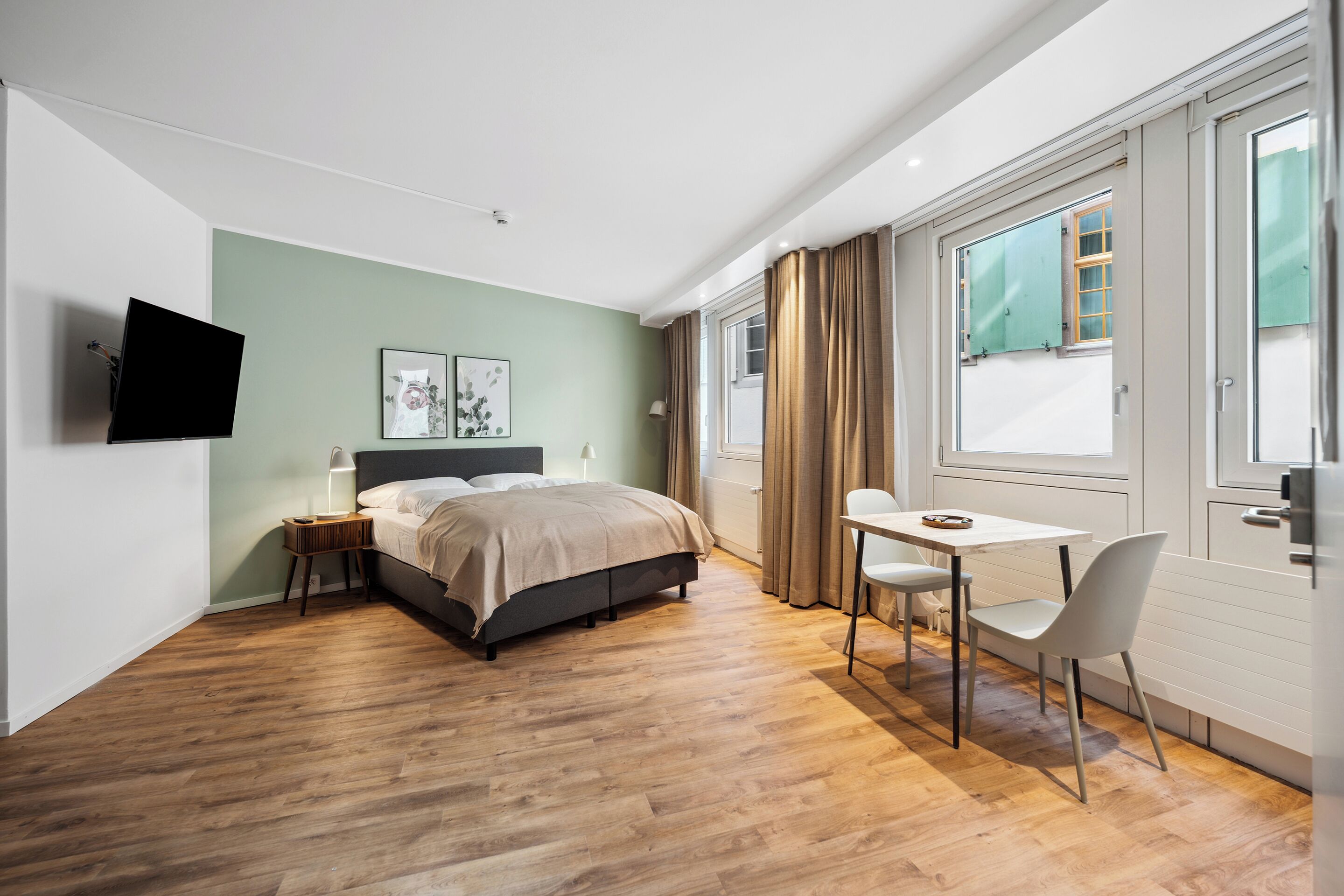 Un dormitorio moderno con cama, mesita de noche y televisor montado en la pared.
