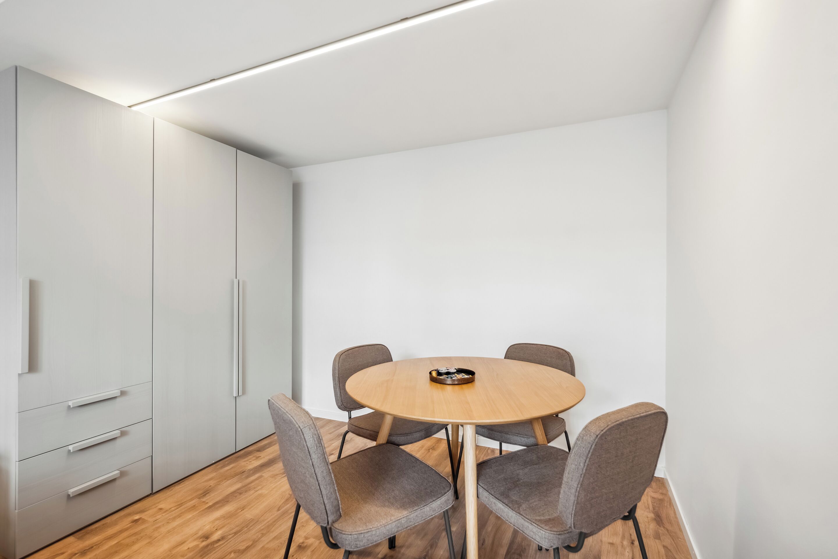 A modern conference room with a round table, four grey chairs, and a white cabinet with drawers.