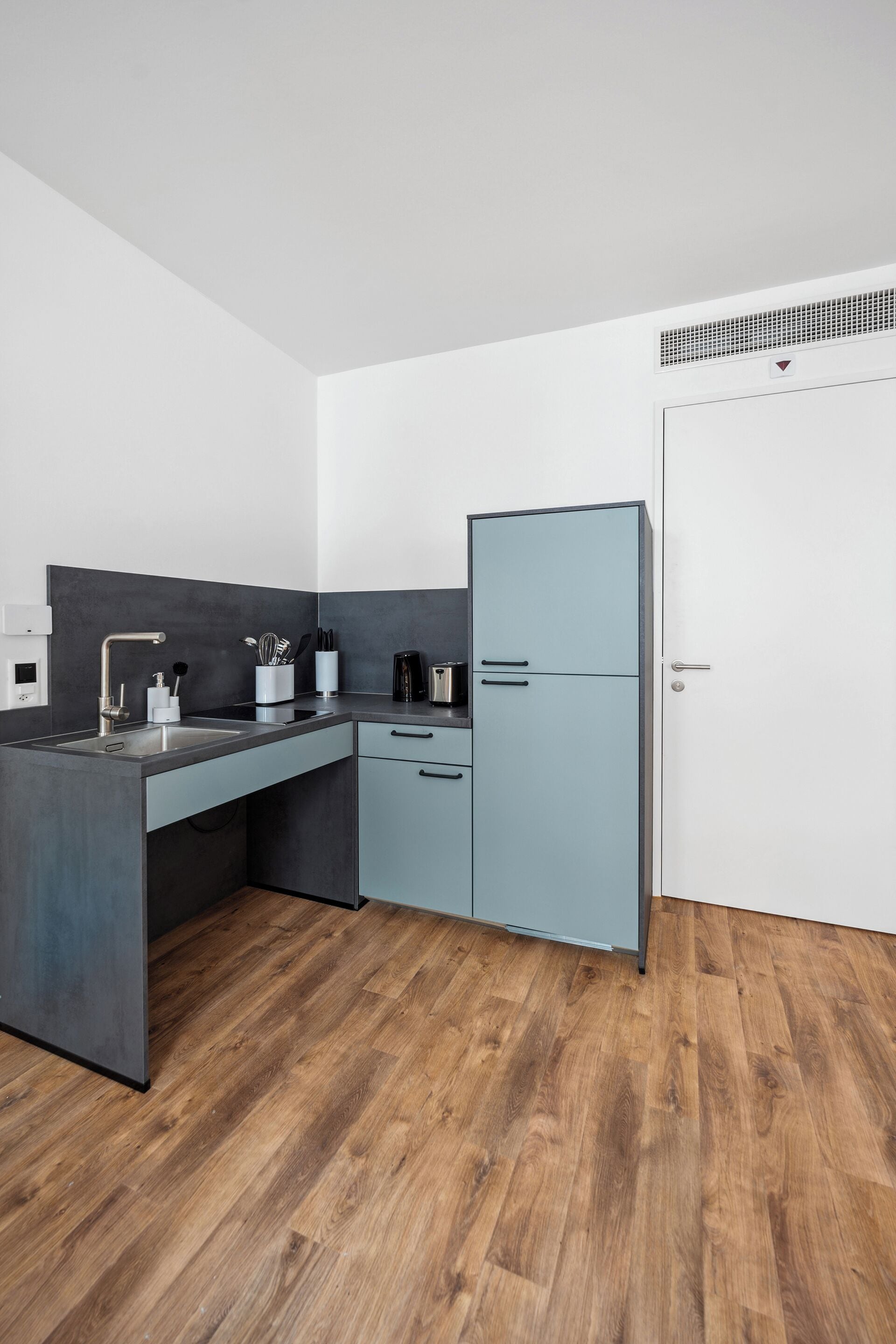 A modern kitchen with a grey countertop, a built-in oven, and a white door.