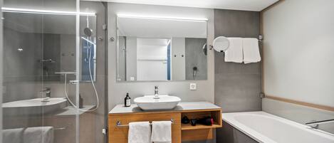 Un baño moderno con ducha de vidrio, tocador de madera con lavamanos y una zona de bañera separada.