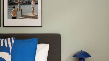 Ein Schlafzimmer mit Bett, Kissen, einem Nachttisch mit Lampe und einem gerahmten Bild an der Wand.