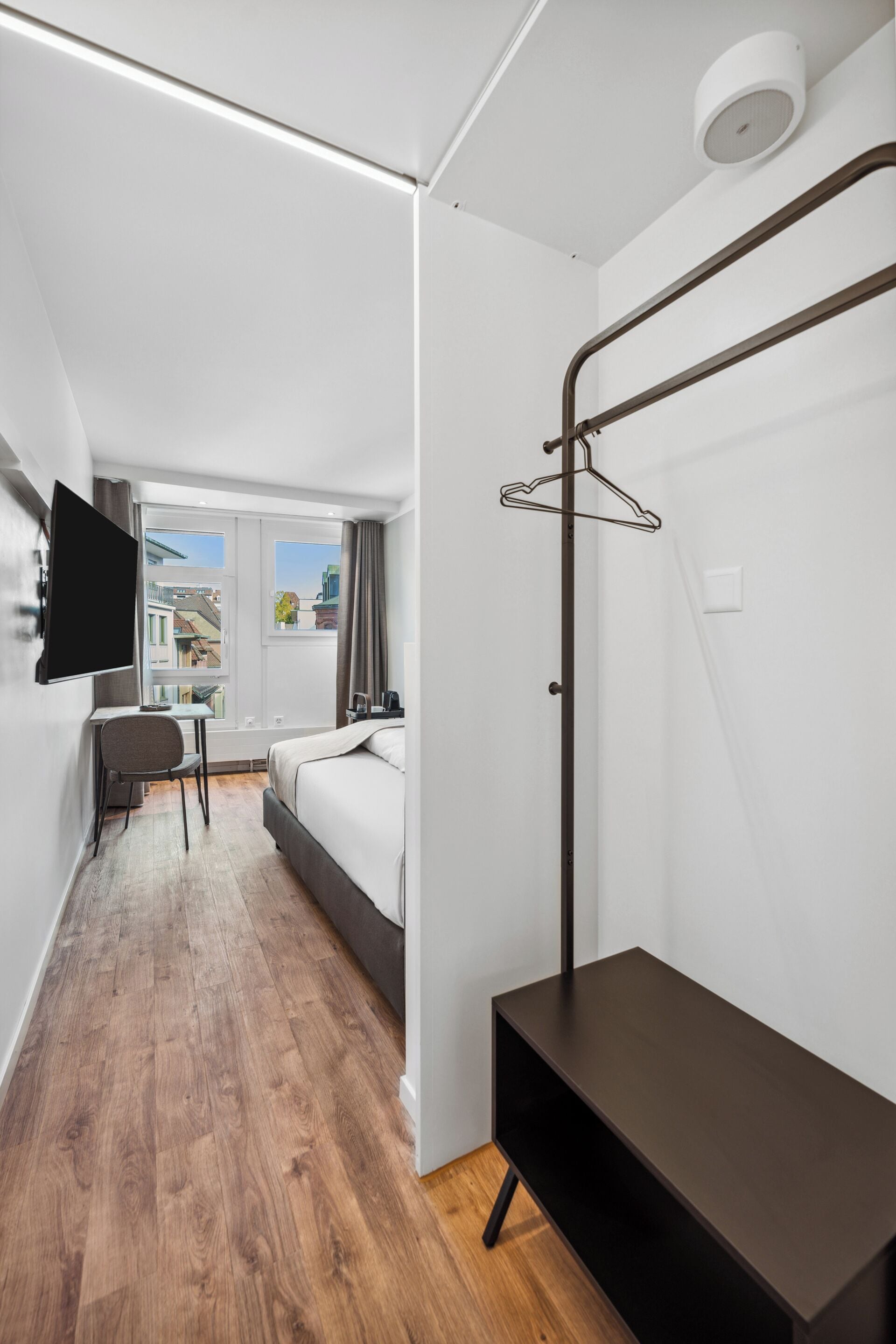 A modern hotel room with a bed, desk, chair, and a TV mounted on the wall.