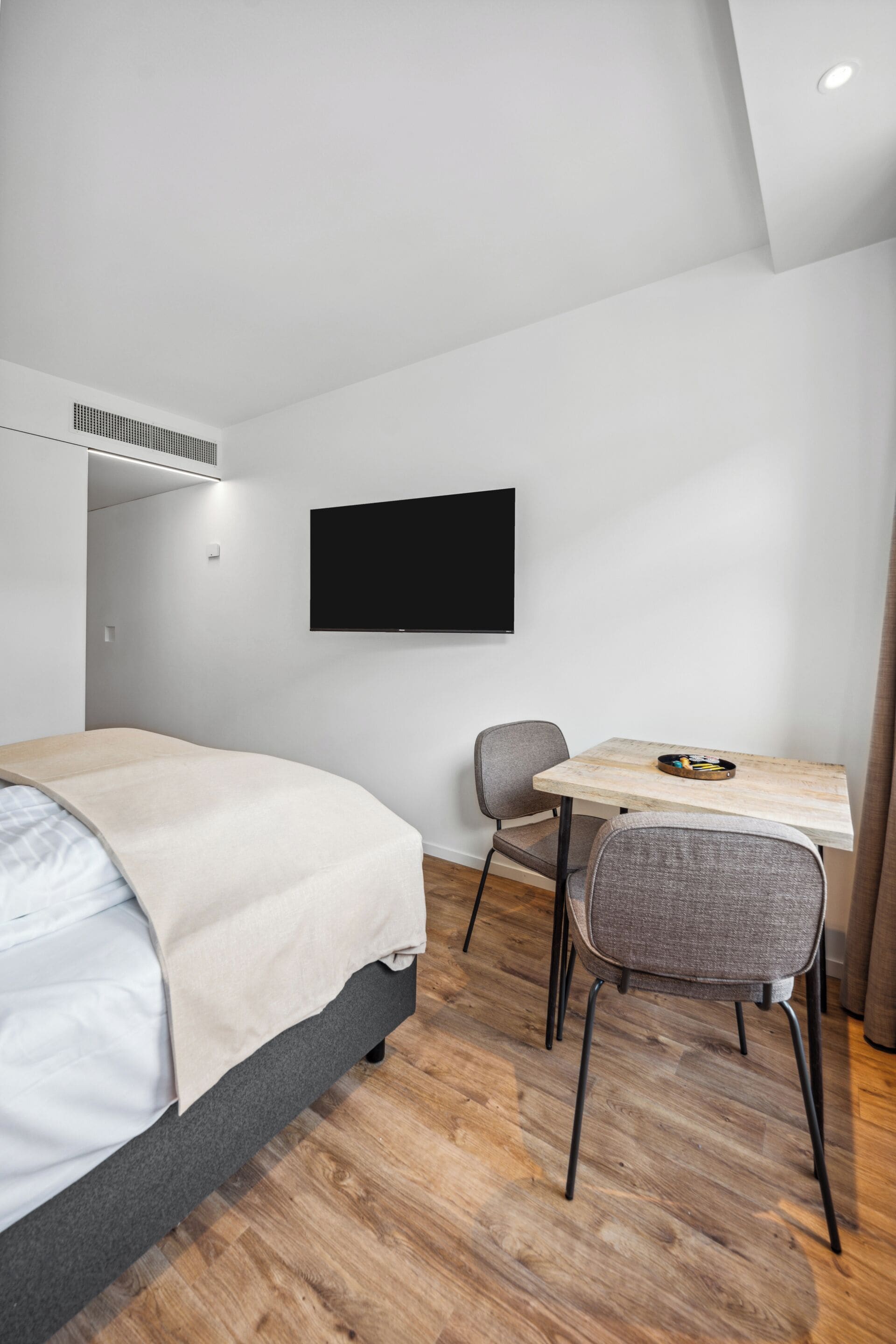 Una habitación de hotel moderna con una cama, un escritorio con una silla, un televisor de pantalla plana y piso de madera.