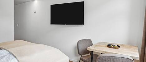 Una habitación de hotel moderna con una cama, un escritorio con una silla, un televisor de pantalla plana y piso de madera.