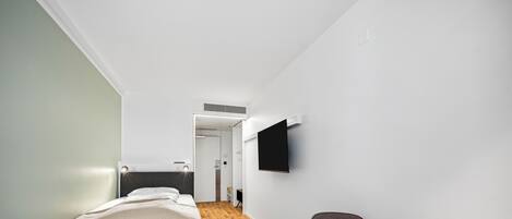 A modern hotel room with a bed, a desk, and a flat-screen TV mounted on the wall.
