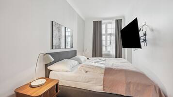 Un dormitorio moderno con cama, mesita de noche, lámpara, obra de arte y televisor montado en la pared.