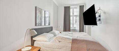 A modern bedroom with a bed, bedside table, lamp, artwork, and a wall-mounted TV.