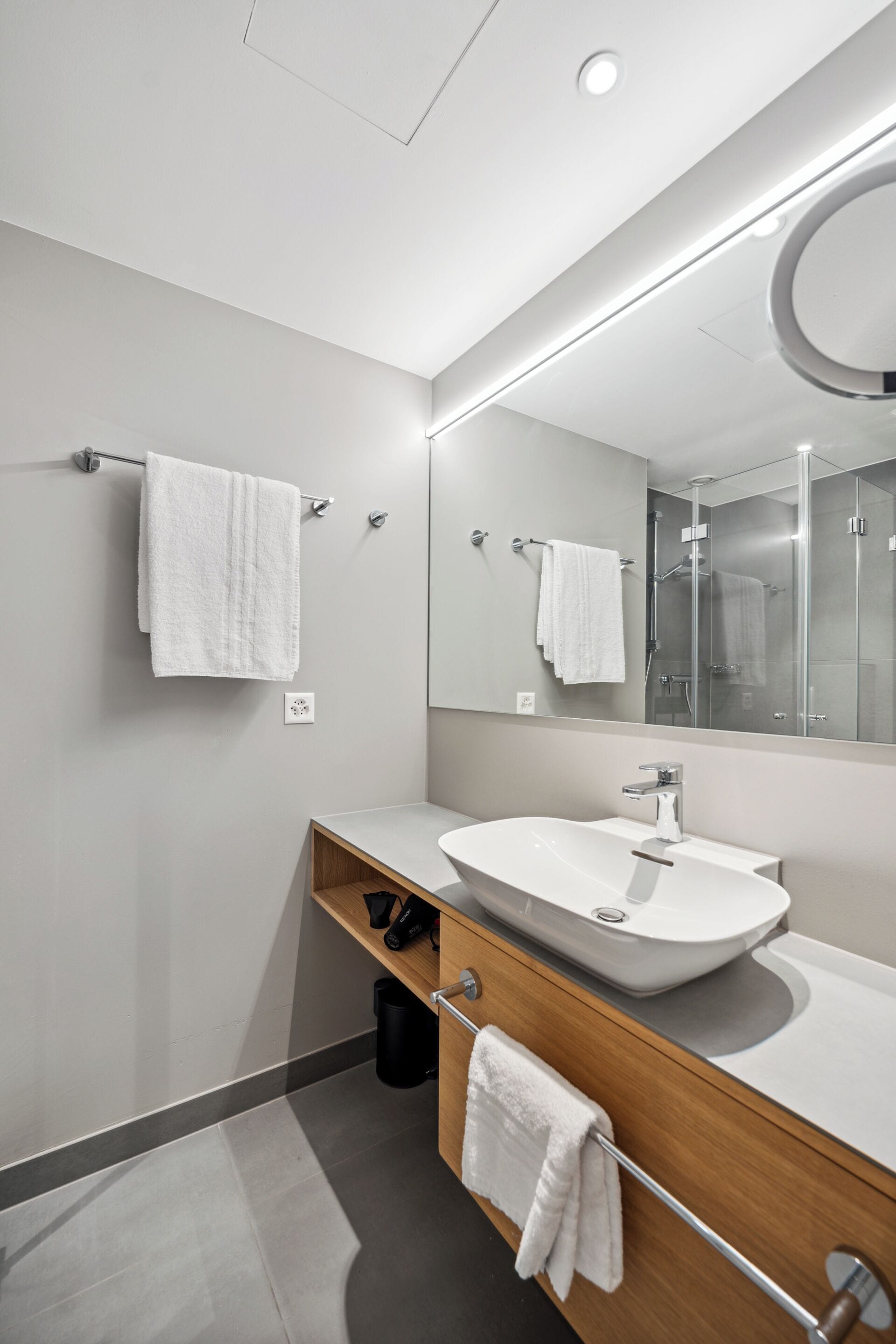 A modern bathroom with a large mirror, white sink, and towel racks.