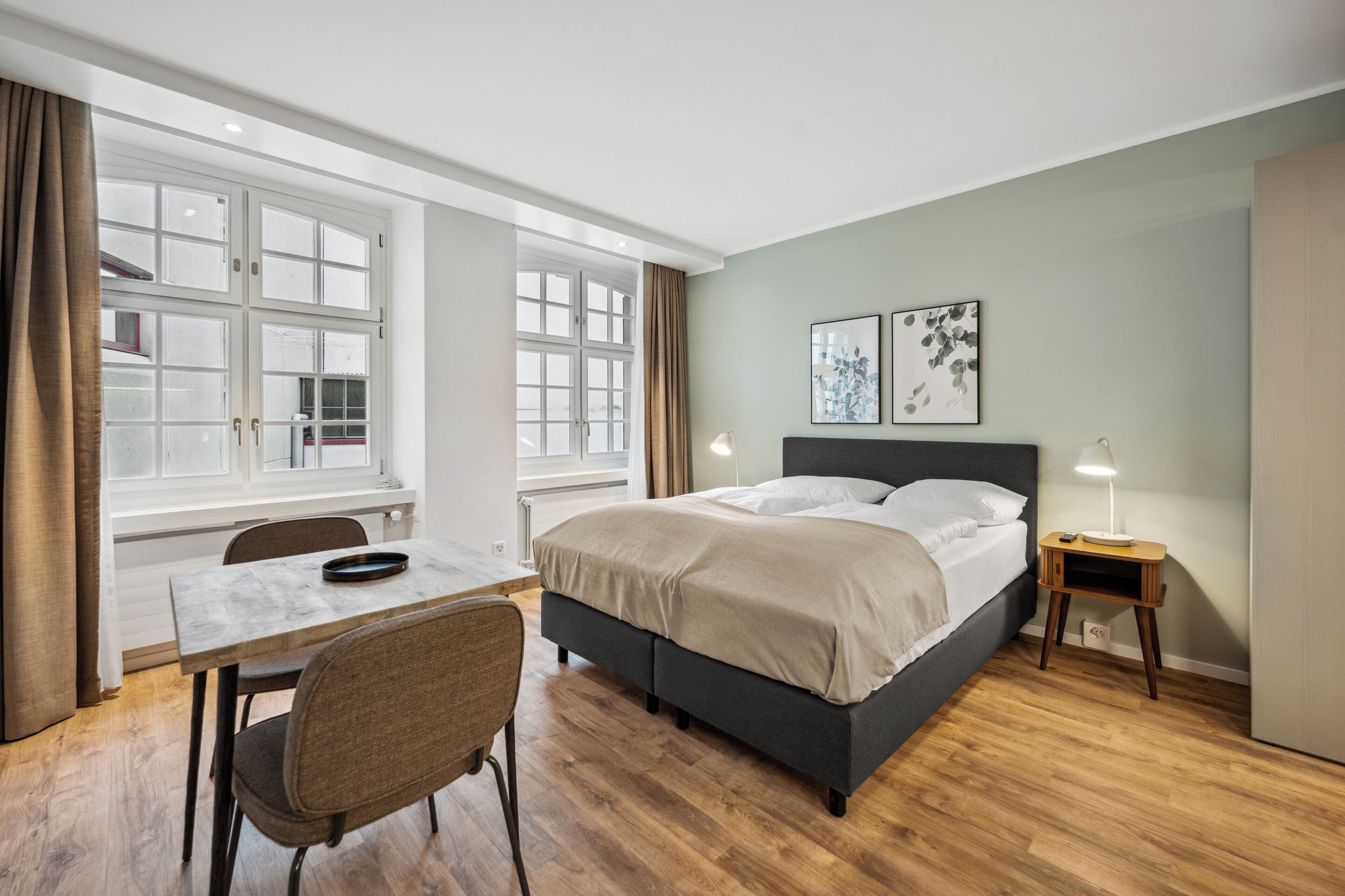 Et soveværelse med seng, sengebord, lampe og et vindue med gardiner.
