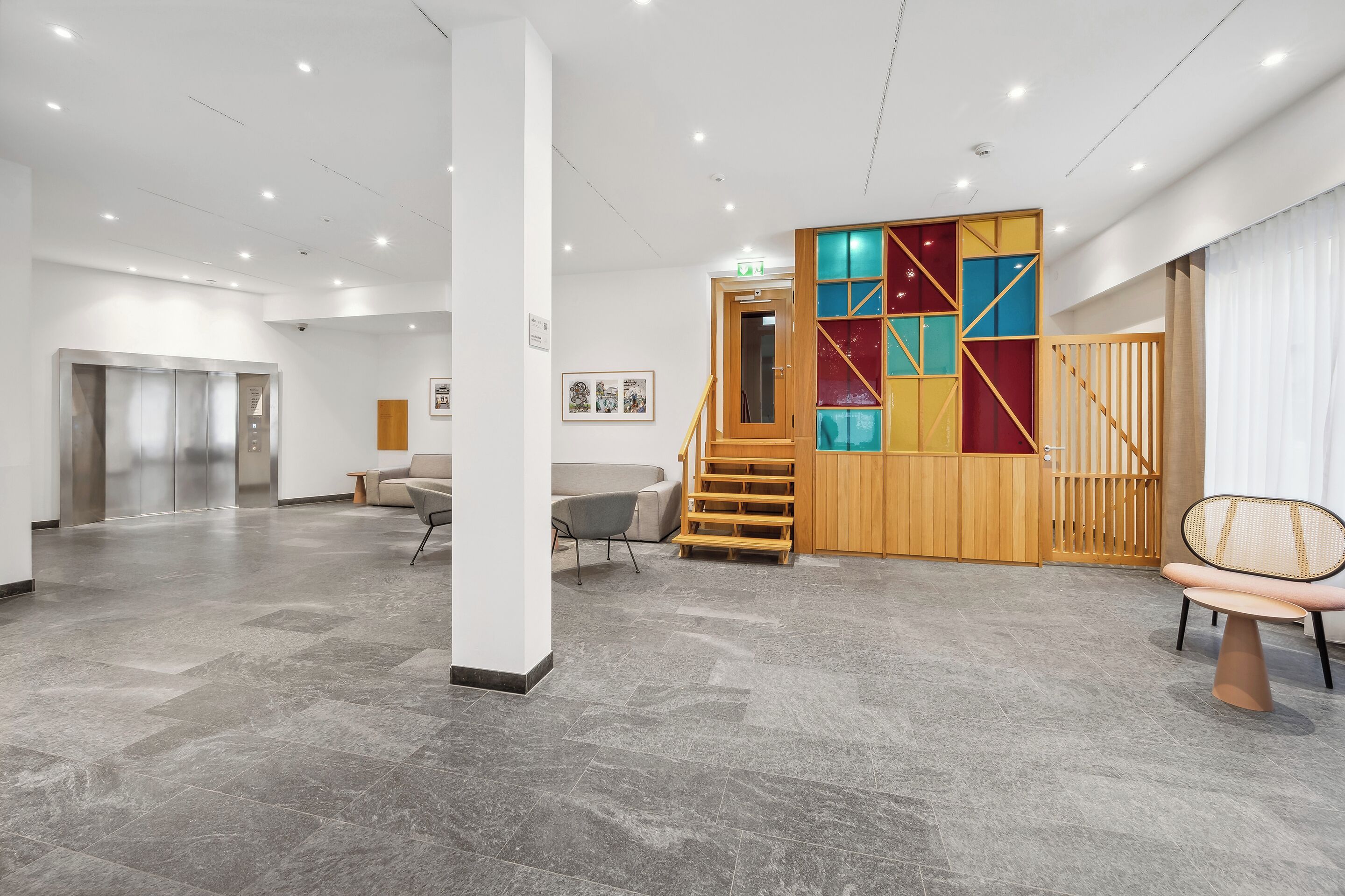 Een ruime lobby met een modern design, met een trap, een zithoek en een receptiebalie.