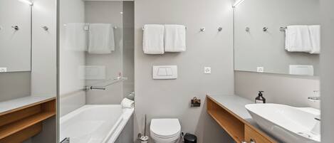 A modern bathroom with a bathtub, toilet, and two sinks.