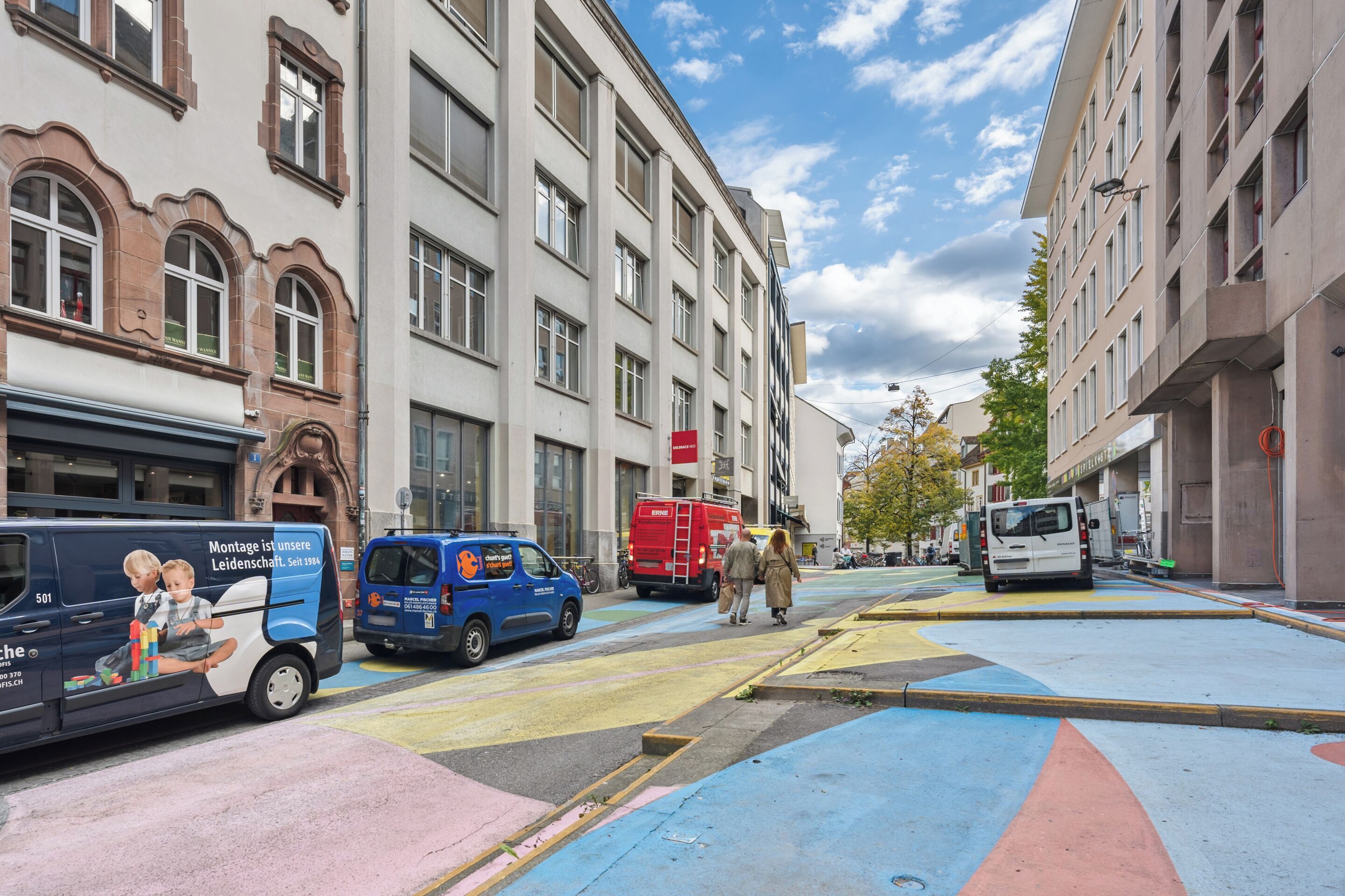 A street with colorful pedestrian crossings, a blue van, and a red delivery truck.