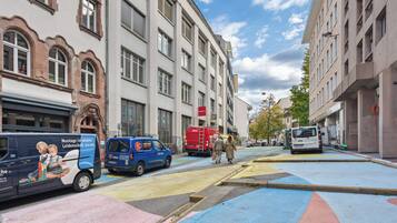 A street with colorful pedestrian crossings, a blue van, and a red delivery truck.