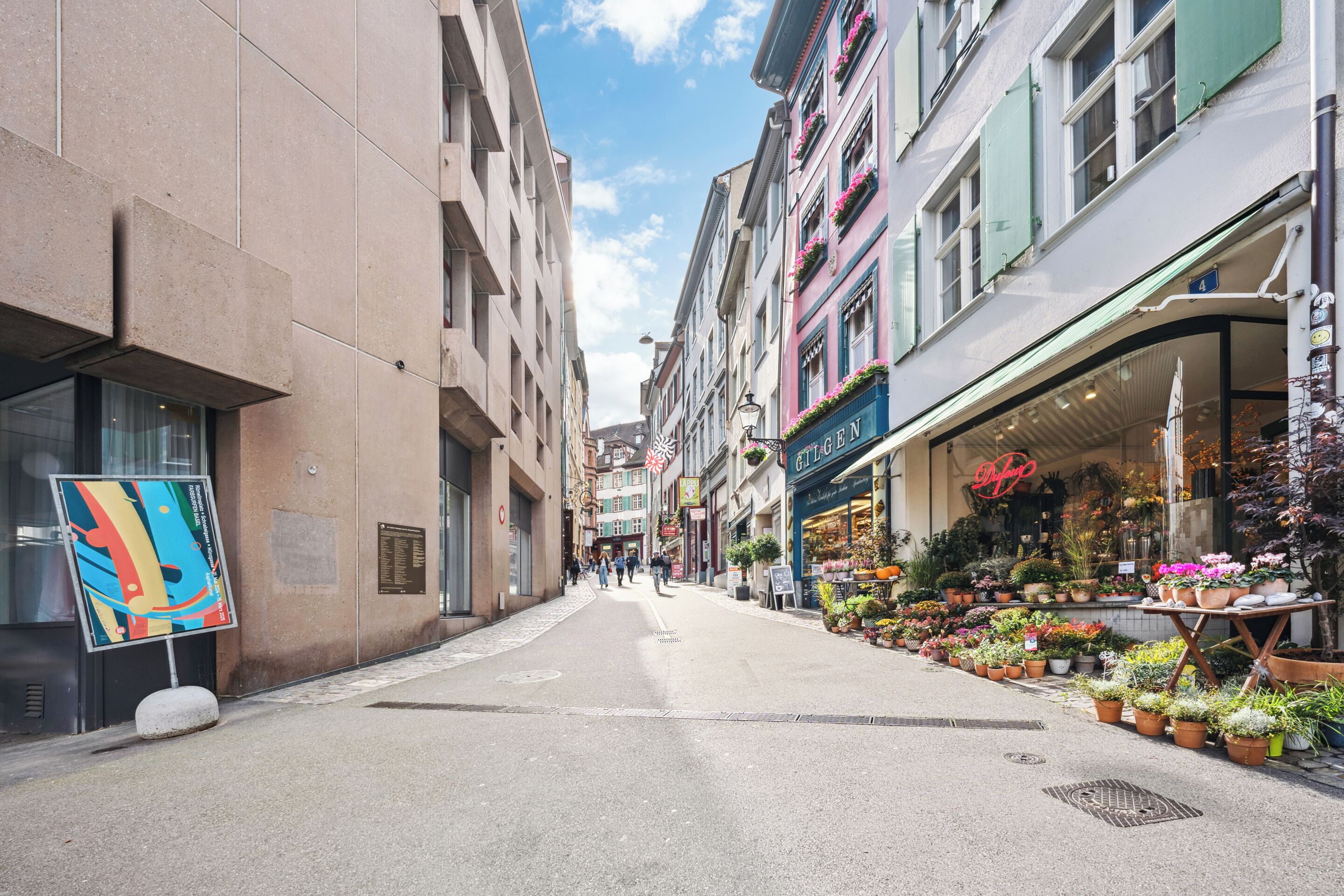 Una stretta via fiancheggiata da edifici, uno dei quali ospita un fiorista.