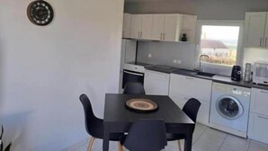 A compact kitchen with white cabinets, a black dining table, and a built-in washing machine. - Apple blossoms (Les Moutiers-en-Cinglais)