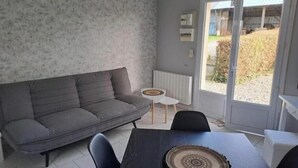 A modern living room with a grey sofa, a small round table, and a dining table with chairs. - Apple blossoms (Les Moutiers-en-Cinglais)