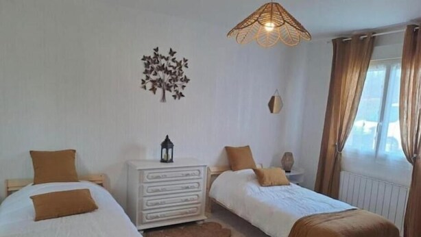 A room with two beds, a white dresser, a decorative wall piece, and a window with curtains. - Apple blossoms (Les Moutiers-en-Cinglais)
