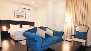 A hotel room with a bed, a blue sofa, a coffee table, and a lamp.