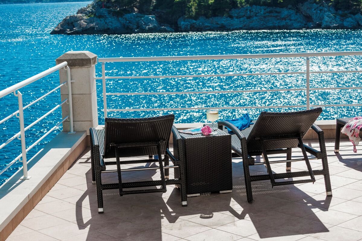 Une terrasse avec deux fauteuils en osier et une petite table, d’où l’on peut admirer une mer d’un bleu éclatant et une côte rocheuse.