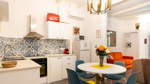 A modern kitchen with white cabinets, a blue and white backsplash, and a dining area with a round table and blue chairs. - Ortigia Courtyard Apartment (Syracuse)