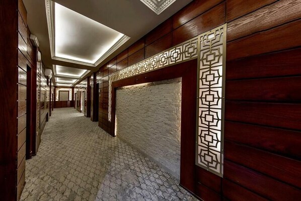 A corridor with wooden paneling and patterned floor tiles, leading to a room with a decorative wall panel.
