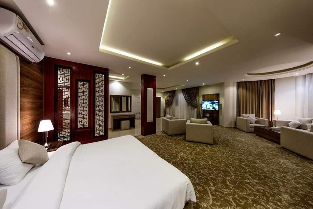 Habitación de hotel con una cama grande, dos sofás, un televisor y un panel decorativo en la pared.