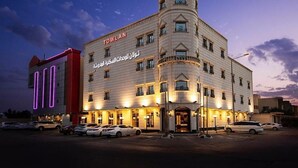 Et hotel med et tydeligt 'TOWLAN' skilt, flere etager og en parkeringsplads med flere biler.