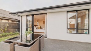 A modern house with a glass door leading to a bedroom, a patio with wicker furniture, and a view of the backyard. - Sunlit Sanctuary with Private Patio in Wigram (Christchurch)