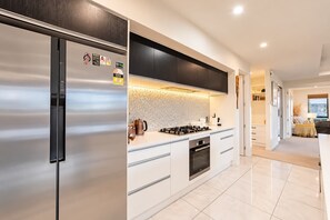 A modern kitchen with a stainless steel refrigerator, a gas stove, and white cabinetry.