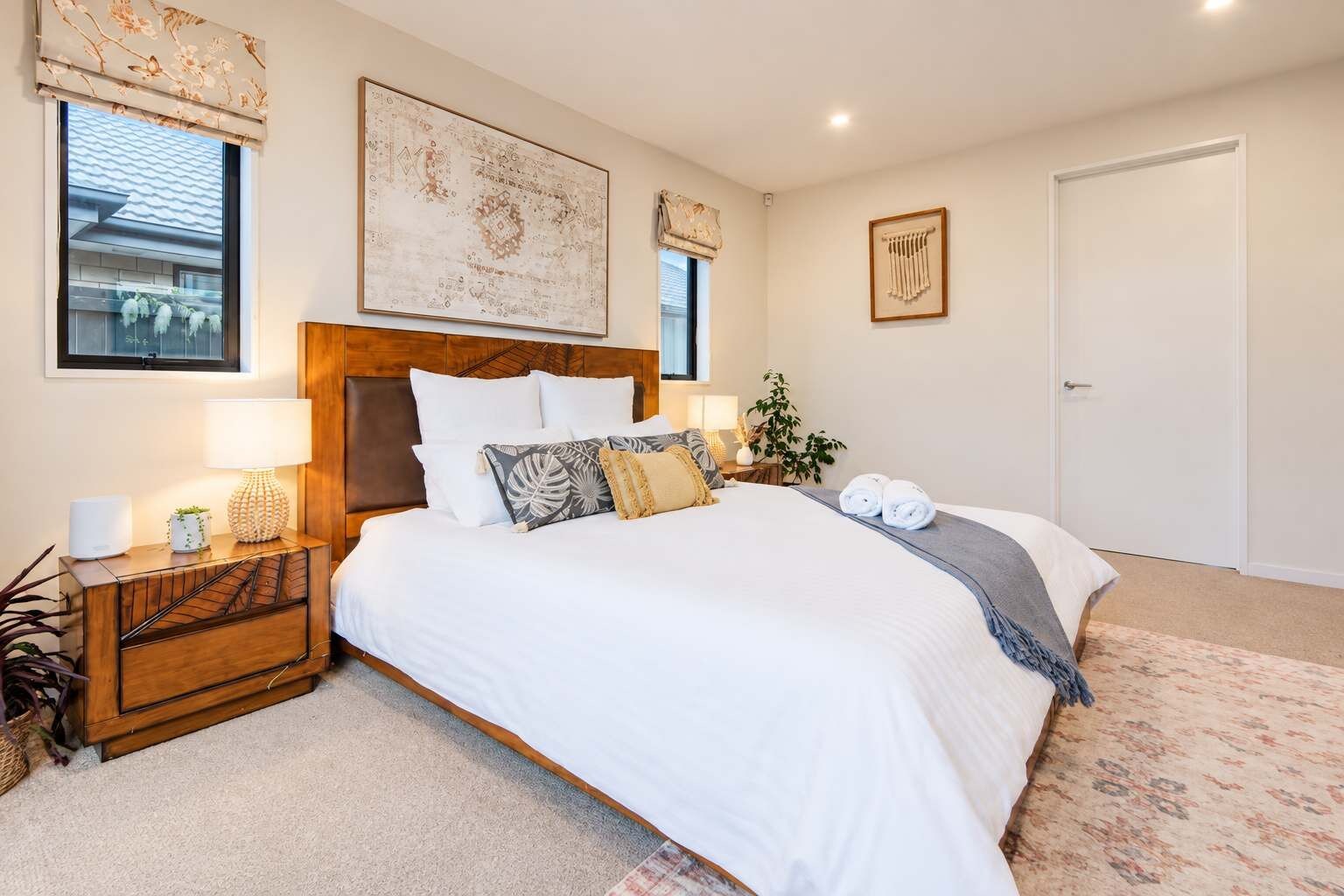 A neatly arranged bedroom with a large bed, a bedside table, a nightstand, and a wall-mounted artwork.