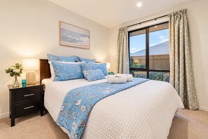 A bedroom with a bed, a nightstand, a lamp, a vase with flowers, and a window with curtains.