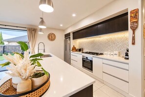 A modern kitchen with a large island, stainless steel appliances, and a decorative backsplash. - Sunlit Wigram Home | 4BR + Patio | Sleeps 8 (Christchurch)