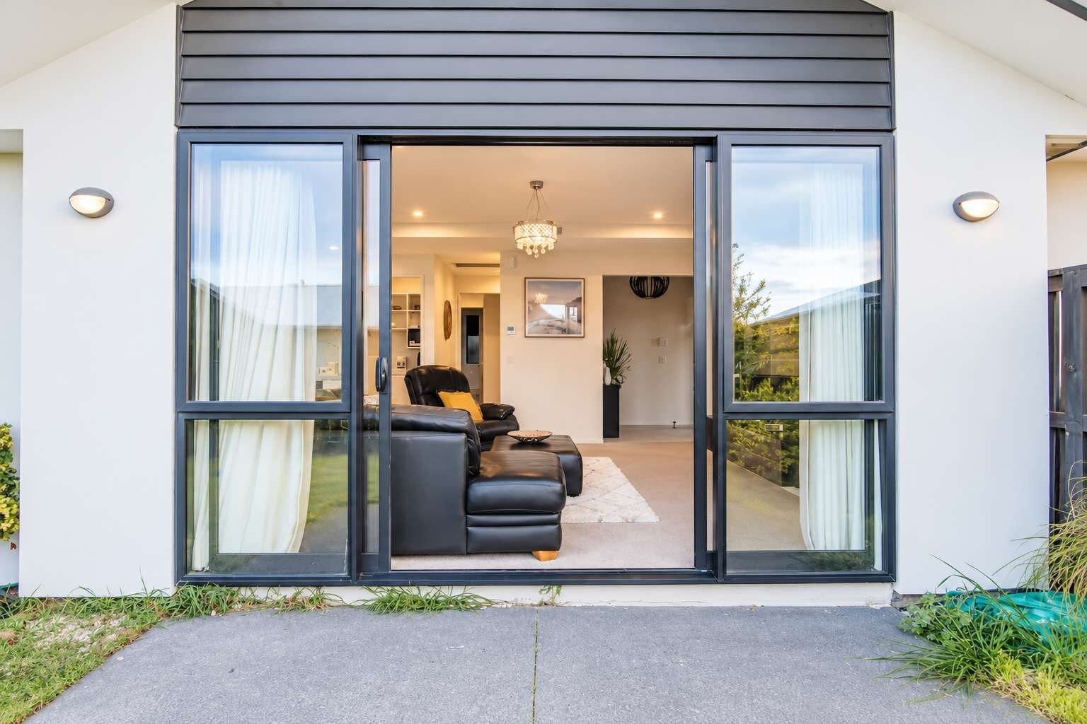 A modern house with a sliding glass door leading to a living area with a sofa and a chandelier.
