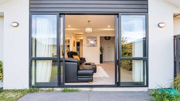 A modern house with a sliding glass door leading to a living area with a sofa and a chandelier.