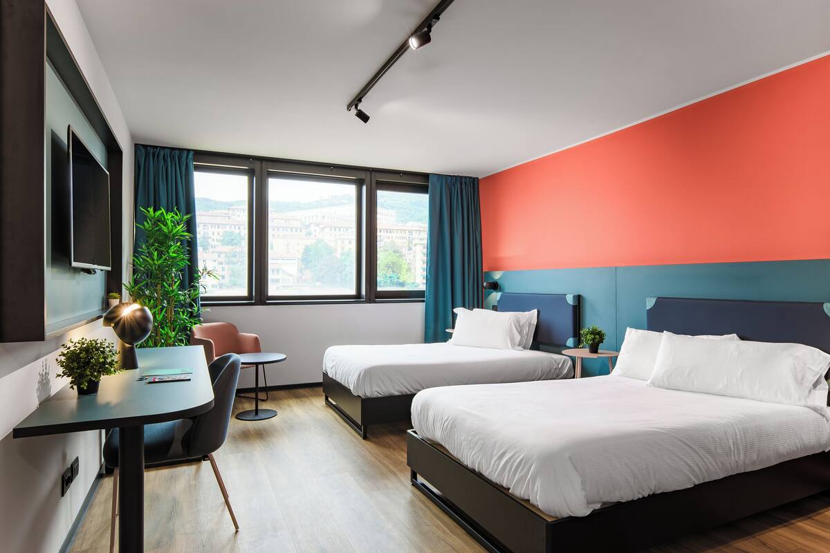 A modern hotel room with two beds, a desk, a chair, and a TV.