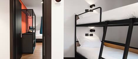 A modern hotel room with a bunk bed, a wooden floor, a small desk with a chair, and a wall-mounted clock.