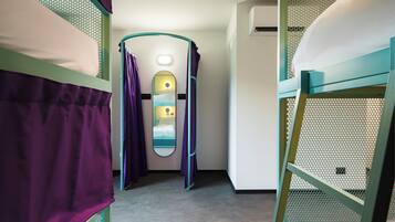 Une chambre avec des lits superposés, un petit miroir et une porte donnant sur une salle de bain.