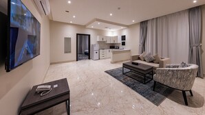 A modern living room with a flat-screen TV, a sofa, a coffee table, and a patterned armchair. - Towlan Qurtuba 2 Serviced Apartments (Riyadh)