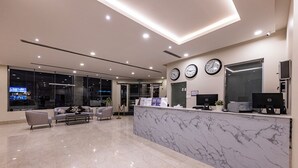 A modern reception area with a marble counter, two clocks, and a seating area with sofas and a coffee table. - Towlan Qurtuba 2 Serviced Apartments (Riyadh)