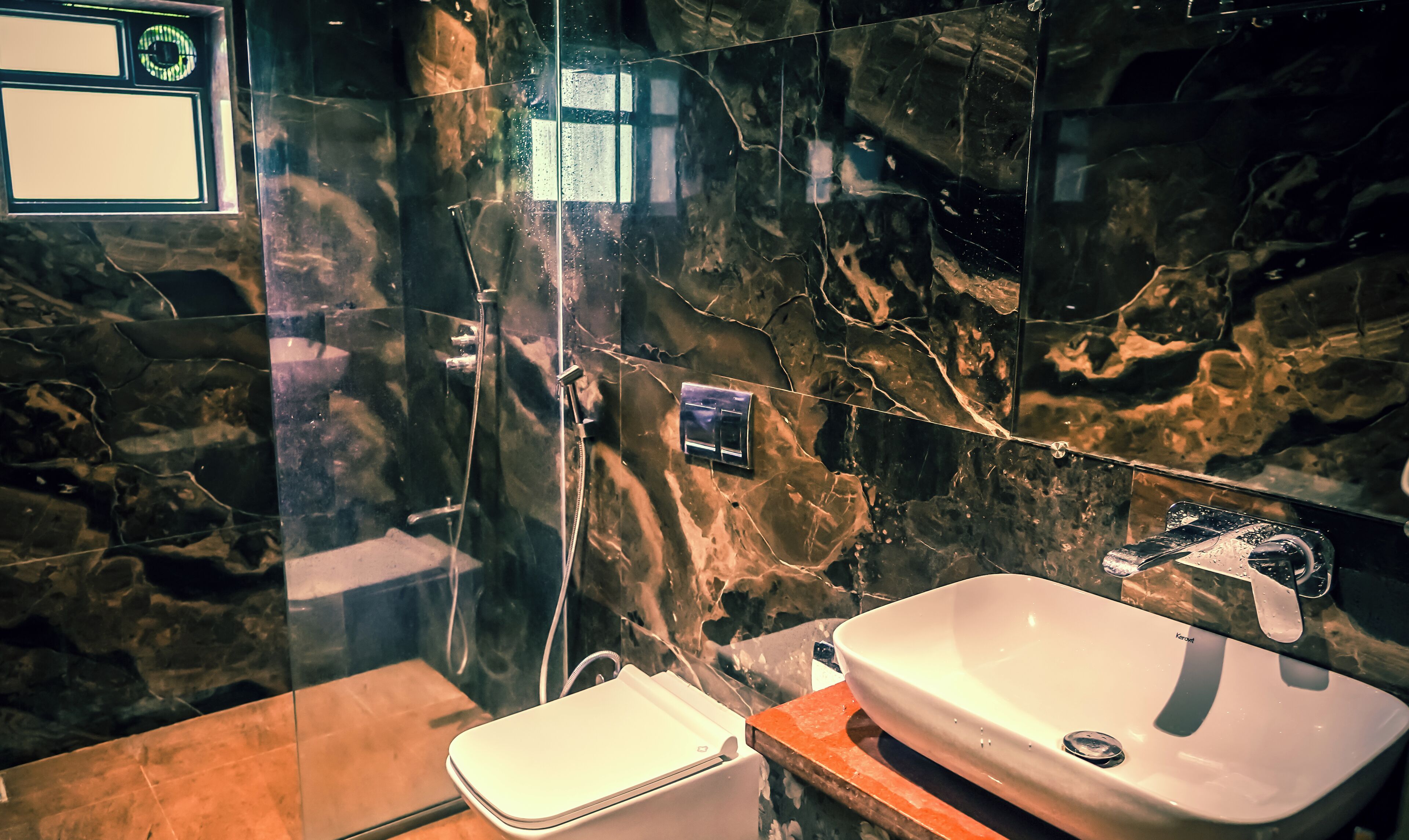 A bathroom with a marble wall, a white sink, and a shower area.