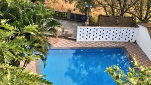 Una piscina rectangular con borde de azulejos y una valla blanca al fondo.